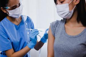 médico trabalhando tinha luvas segurando seringa e fazendo injeção para paciente mulher asiática com máscara médica. vacina covid-19 ou coronavírus