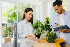 homem e mulher asiáticos verificam e embalam planta pequena, vendendo árvore purificadora de ar verde foto