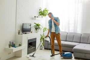 jovem bonito e bonito caucasiano aspirando apartamento moderno, limpeza, governanta, cara fazendo tarefas domésticas e limpa sala de estar usando aspirador de pó, limpeza doméstica foto