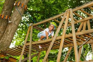 menina da escola feliz desfrutando de atividade em um parque de aventura escalada num dia de verão foto