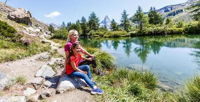 mulher e menina alpinista feliz no lago de montanhas foto