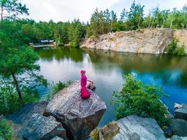 alpinista com mochila relaxando em uma rocha e apreciando o pôr do sol foto