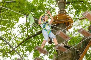 menina da escola feliz desfrutando de atividade em um parque de aventura escalada num dia de verão foto