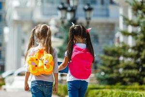 duas meninas da escola usando mochila fora da escola primária. colegial, estudante do ensino fundamental indo da escola, formatura, férias de verão. foto