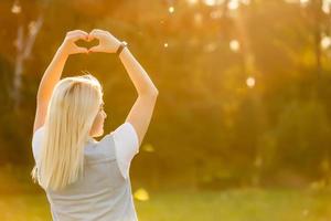 uma jovem fazendo o símbolo do coração com as mãos ao pôr do sol
