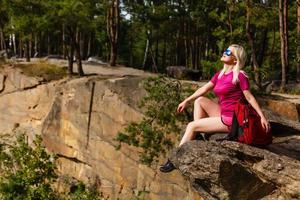 alpinista com mochila relaxando em uma rocha e apreciando o pôr do sol foto