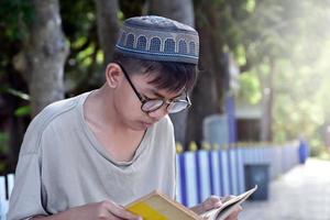 jovem muçulmano asiático usa óculos, sentado no parque da escola e lendo seu livro em seus tempos livres antes de voltar para casa, foco suave e seletivo. foto