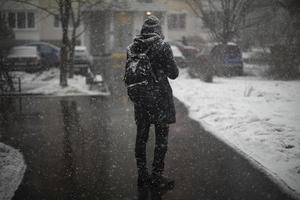 homem lá fora na queda de neve. roupas pretas na neve. cara está parado no meio da cidade. foto