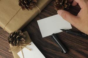 mãos masculinas embrulhando presentes de ano novo e escrevendo cartões em uma mesa de madeira marrom, vista superior, flatlay foto