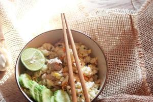 arroz frito de porco, arroz frito à moda chinesa em uma tigela com pepino e limão servido em uma mesa de madeira marrom. foto