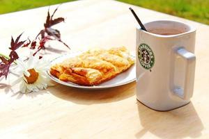 washington, eua - 01 de agosto de 2022 caneca de café com logotipo da starbucks na frente, padaria branca no prato. coloque-o sobre uma mesa de madeira no jardim onde o sol da manhã brilha. foto