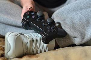 controlador de jogo preto moderno nas mãos de uma jovem sentada foto