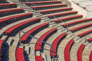 cadeiras de plástico vermelhas vazias nas arquibancadas do estádio ou anfiteatro. muitos assentos vazios para espectadores nas arquibancadas. foto