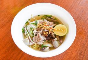 tigela de macarrão delicioso perto de sopa de macarrão aletria picante com ensopado de carne de porco vegetal e limão na tigela comida tradicional tailandesa e chinesa da ásia, miudezas de porco, intestinos de porco fígado foto