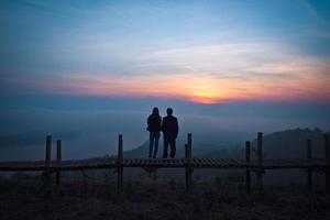vista na silhueta de casal amante de colina em pé sobre uma ponte de madeira foto