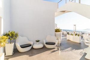 terraço branco no hotel de luxo, ilha de santorini. luxuoso restaurante e recepção do hotel. interior branco, cadeiras e mesa, céu azul suave e clima ensolarado foto