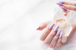 mãos de menina com manicure roxa delicada e flores de orquídea foto