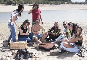 verão, feriados, férias, música, conceito de pessoas felizes - grupo de amigos com guitarra se divertindo na praia foto