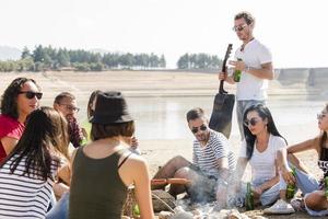 verão, feriados, férias, música, conceito de pessoas felizes - grupo de amigos com guitarra se divertindo na praia foto