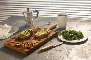abacate fatiado no pão torrado com nozes e café. espinafre em um prato e pote de moka. café da manhã e conceito de comida saudável. foto