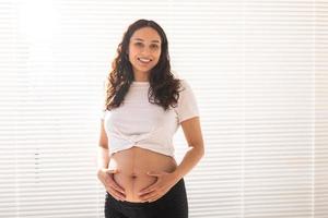 sorrindo linda jovem grávida tocando sua barriga e regozijando-se. conceito de sentimentos positivos e agradáveis enquanto espera o bebê. copie o espaço foto