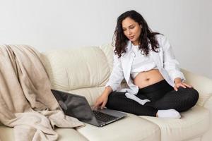 mulher grávida usando laptop enquanto está sentado em um sofá na sala de estar em casa foto