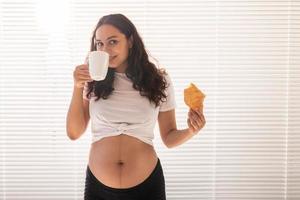 mulher grávida comendo croissant e bebe café. gravidez e licença maternidade foto