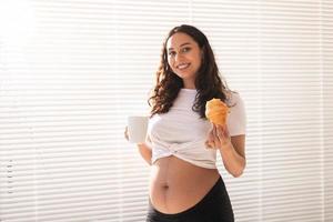 mulher grávida feliz com pães de croissant em casa. gravidez, alimentação e conceito de pessoas foto
