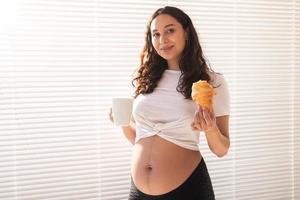 mulher grávida feliz com pães de croissant em casa. gravidez, alimentação e conceito de pessoas foto