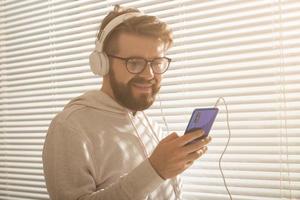 retrato de close-up do homem jovem elegante hipster escolhendo música favorita em smartphone com fones de ouvido no escritório. conceito de assinatura de música foto