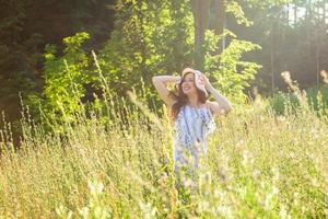 jovem feliz com cabelos longos no chapéu e vestido andando pela floresta de verão em um dia ensolarado. conceito de alegria de verão foto
