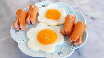 café da manhã com ovo frito em forma de flor e linguiça fatiada no prato ou prato na mesa de mármore ou fundo branco e copie o espaço. fechar comida foto