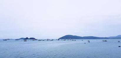 muitos barcos de cauda longa e lanchas no mar. veículo no oceano com céu branco e fundo de montanha com espaço de cópia em cima ou acima. paisagem de exibição em phuket, tailândia. viagem e viagem. paisagem marinha foto