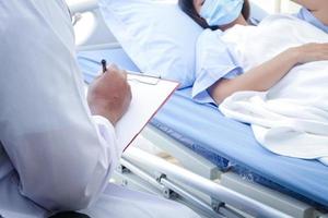 médico afro-americano verifica a doença de uma mulher deitada em uma cama de hospital. tratamento de pacientes durante a epidemia de coronavírus. conceito de serviço médico. foto