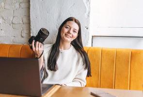 morena sorridente jovem fotógrafa trabalhando com sua câmera e laptop no café foto