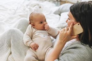 mãe falando no celular com menino fofo na cama, tons naturais, emoção de amor foto