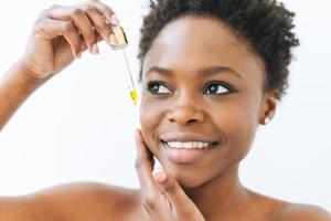 retrato da beleza de uma jovem africana sorridente em cueca com óleo cosmético para rosto em fundo branco foto