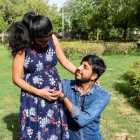 casal indiano posando para ensaio de maternidade. o casal está posando em um gramado com grama verde e a mulher está vacilando sua barriga no jardim lodhi em nova delhi, índia foto