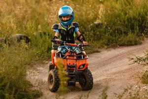 um garotinho usando um capacete andando de quadriciclo na margem de um rio de montanha. foto