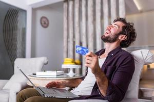 conceito de tecnologia, compras, serviços bancários, casa e estilo de vida - close-up do homem com computador portátil e cartão de crédito em casa. jovem usando cartão de crédito para fazer compras online. foto