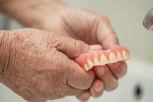 paciente idosa asiática segurando e lavando dentadura na enfermaria do hospital de enfermagem conceito médico forte e saudável foto