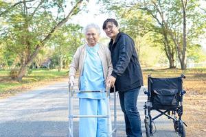 cavergiver ajuda e cuida da senhora asiática sênior ou idosa com saúde forte enquanto caminhava no parque em um feriado feliz e fresco. foto