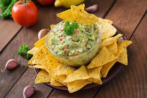 abacate guacamole, limão, tomate, cebola e coentro, servido com nachos - lanche mexicano tradicional foto