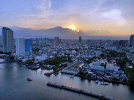 vista aérea de um pequeno rebocador rebocando uma grande barcaça de areia, barco de areia carregando carga de areia no rio chao phraya em bangkok, tailândia, crepúsculo foto