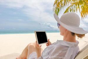 jovem de chapéu com tablet pc na praia. cenário de praia tranquilo perfeito, mulher relaxada trabalhando como home office. cenário maravilhoso da natureza na praia tropical. copie o espaço para texto, verão ensolarado foto