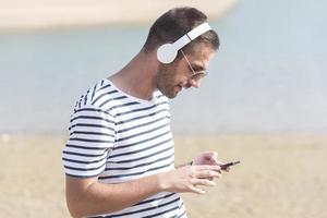 homem com fones de ouvido ouvindo música com seu smartphone à beira do lago foto