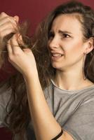 cabelo danificado. bela jovem triste com cabelos longos desgrenhados. retrato do close up do modelo fêmea que prende o cabelo seco não escovado bagunçado nas mãos. danos capilares, conceito de saúde e beleza. alta resolução foto