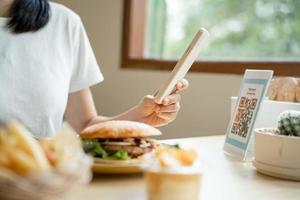 a mão de uma mulher usa um telefone para digitalizar um código qr em um restaurante para receber um desconto ou pagar por comida. use o telefone para transferir dinheiro ou pagar online sem dinheiro. foto