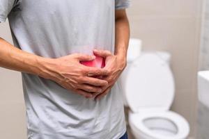 homem em pé tem diarréia e comida severamente tóxica. homem toca barriga no banheiro. dor abdominal, diarréia, conceito de câncer de cólon foto