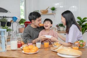 atividades juntos durante as férias. pais e filhos estão fazendo uma refeição juntos durante as férias. menino está provocando seu pai, dando-lhe pão e legumes. foto